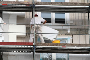 Bauarbeiter auf Gerüst trägt Dämmmaterial auf Wand auf